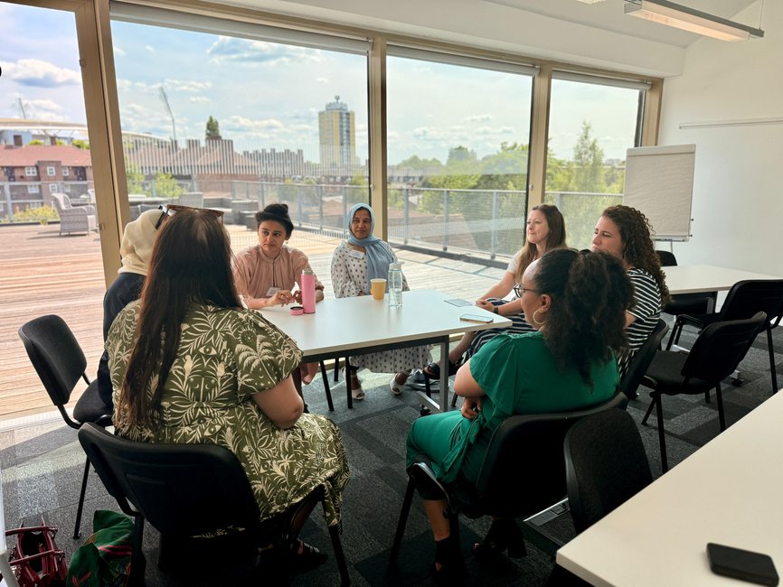 a group of women sitting round a table in front of a large window